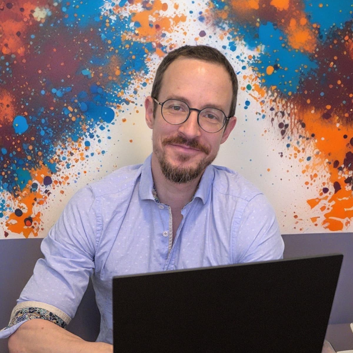 Professional headshot of CEO with laptop against vibrant blue and orange artistic paint splatter background